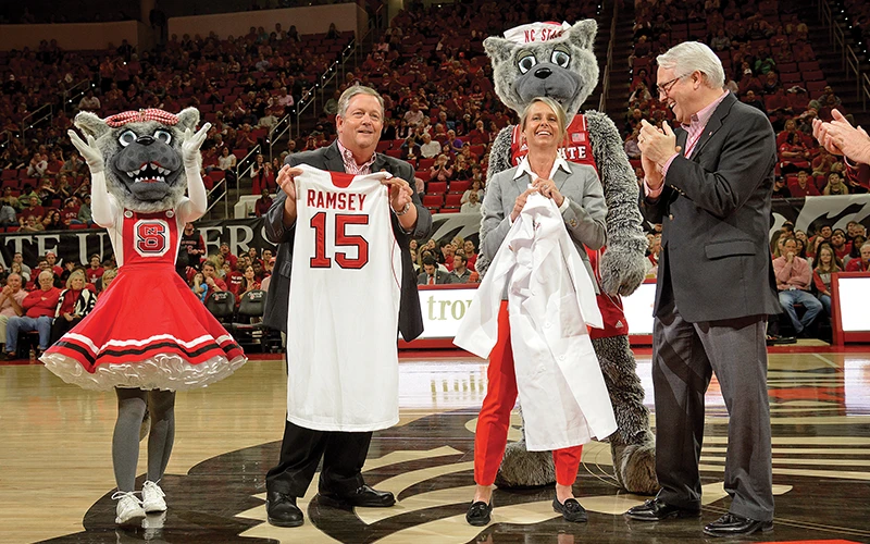 Randy Ramsey honored at an NC State University basketball game, holding a personalized jersey, recognizing his contributions